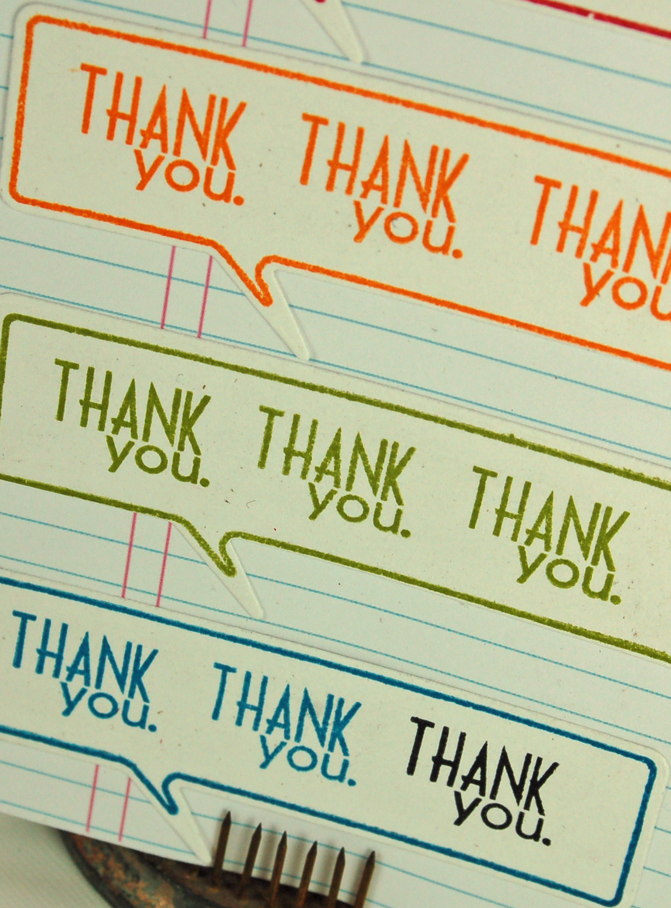 close up of card front that is covered in what looks like regular lined paper with multiple talk bubble stamps that say thank you in rainbow colors